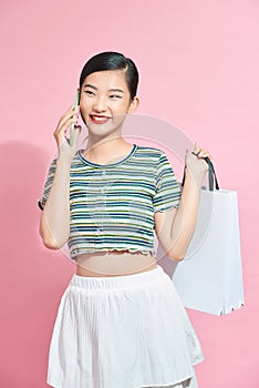 Beautiful Attractive Asian Woman holding shopping bags and calling with mobile phone isolated on pink background