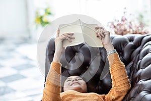 Beautiful Attractive Asian woman lying on sofa in living room reading book