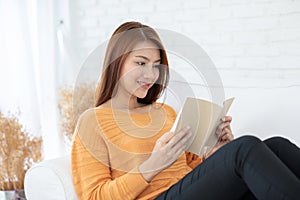 Beautiful Attractive Asian woman lying on sofa in living room reading book for learn and education smile and positive thinking