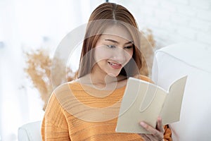 Beautiful Attractive Asian woman sitting on sofa in living room reading book