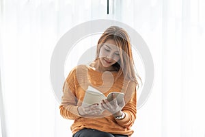 Beautiful Attractive Asian woman sitting on sofa in living room reading book