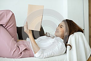 Beautiful Attractive Asian woman sitting on sofa in living room reading book for learn and education