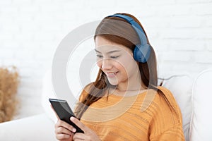Beautiful Attractive Asian young woman listen music lying on sofa and using smartphone to playing social media in living room