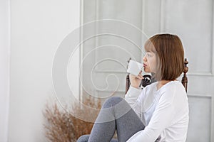 Beautiful Attractive Asian young woman sitting on wooden chair and relax with coffee after wake up in the morning