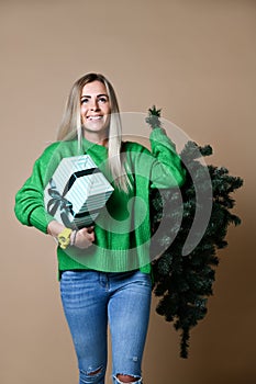 Beautiful attractive blond hair woman hold Christmas fir tree with bokeh lights and gift box in green sweater