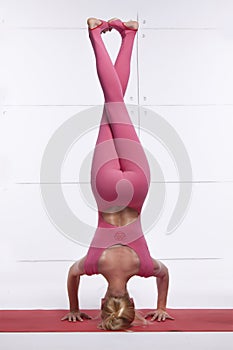 Beautiful attractive blond woman doing yoga standing on his head with legs crossed relaxes and opens the chakra dressed in co