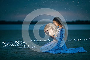 Beautiful attractive girl on a night beach with sand and stars hugs the moon, Artistic Photography