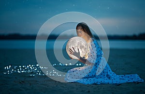 Beautiful attractive girl on a night beach with sand and stars hugs the moon, Artistic Photography