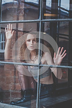 Beautiful attractive woman with curly hait and grey top touching window glass