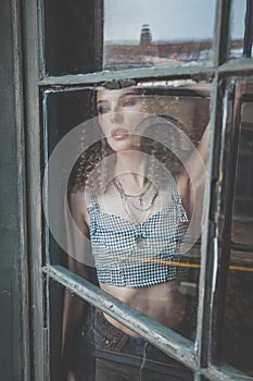 Beautiful attractive woman with curly hait staying by the window