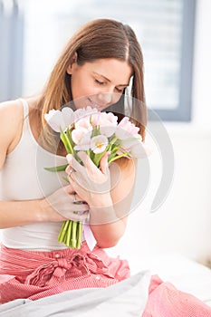 Beautiful attractive woman sitting on the bed holding tenderly in hands a bouquet of spring tulips