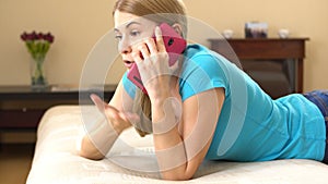 Beautiful attractive young woman in a blue t-shirt lying on sofa and talking on the phone.