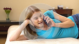 Beautiful attractive young woman in a blue t-shirt lying on sofa and talking on the phone.