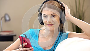 Beautiful attractive young woman in a blue t-shirt sitting on sofa and listening to the music.