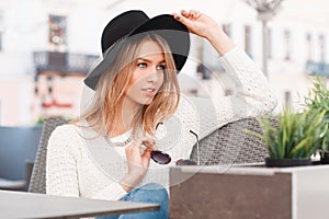 Beautiful attractive young woman in a knitted white sweater in jeans in a stylish elegant hat sitting on a sofa at a gray table