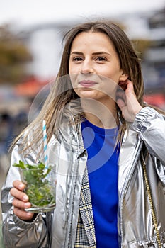 Beautiful attractive young woman or twentysomething girl drinking cold mojito with straw in city center during happy photo