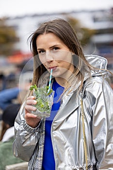 Beautiful attractive young woman or twentysomething girl drinking cold mojito with straw in city center during happy photo