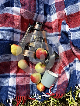 Beautiful autumn composition with vintage lantern, mug, coffee turk, blue red wool blanket, apples and pears, camping, picknic