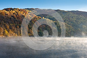 Beautiful autumn forest in the morning, fog over lake