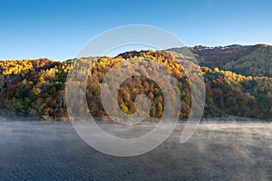 Beautiful autumn forest in the morning, fog over lake