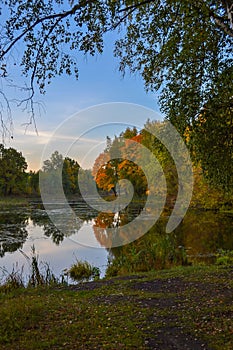 Beautiful autumn landscape. Lake, yellow and red trees by the lake. Reflection in water. Blue sky. Sunny autumn day