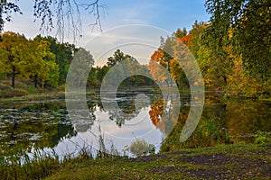 Beautiful autumn landscape. Lake, yellow and red trees by the lake. Reflection in water. Blue sky. Sunny autumn day