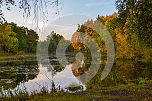 Beautiful autumn landscape. Lake, yellow and red trees by the lake. Reflection in water. Blue sky. Sunny autumn day