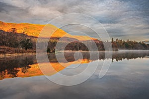 Beautiful Autumn landscape sunrise image looking towards Catbells from Manesty Park in Lake District with mist rolling across the