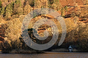 Beautiful Autumn landscape sunrise image of Rydal Water boathouse in Lake District with sunlight kissing the treetops photo