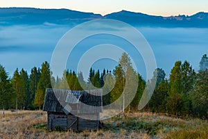 Beautiful autumn landscape during sunrise with old hut and fog in valley with mountains, Romania