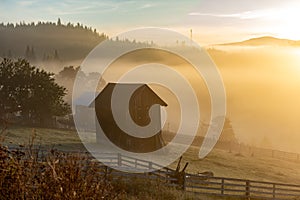 Beautiful autumn landscape during sunrise with old hut and fog in valley with mountains, Romania