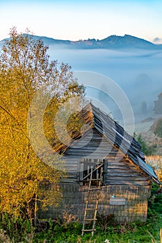 Beautiful autumn landscape during sunrise with old hut and fog in valley with mountains, Romania