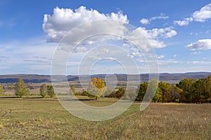 Beautiful autumn landscape of a valley in a mountainous area. Sunny day and white clouds on a blue sky