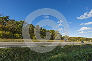 Beautiful autumn landscape view. Asphalt road on yellowed trees and blue sky white white clouds background