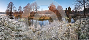 Beautiful autumn morning panorama with frosty grass, small river, falling trees and blue sky.