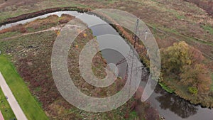 Beautiful autumn nature with small river and transmission electricity  tower against forest. Drone flying above creek at autumn