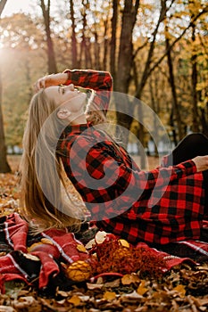 Beautiful autumn portrait of young woman with long natural blonde hair with yellow leaves in red checkered dress. Romantic Girl