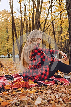 Beautiful autumn portrait of young woman with long natural blonde hair with yellow leaves in red checkered dress. Romantic Girl