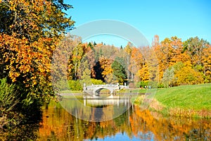 Beautiful autumn sunny landscape with the bridge over Slavyanka river and trees with red and orange leaves, Pavlovsk, St