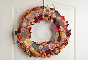Beautiful autumnal wreath with flowers, berries and fruits hanging on white wooden door. Space for text