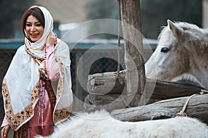 Beautiful azeri woman in traditional Azerbaijani dress standing with white horse photo