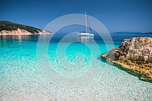 Beautiful azure blue lagoon with sailing catamaran yacht boat at anchor. Pure white pebble beach, some rocks in the sea