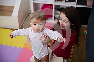 Beautiful baby boy in the hands of his loving caring sister. Cute child girl supporting her brother doing first steps