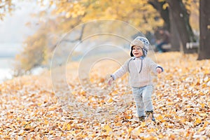 Beautiful baby boy walking throw the autumn leaves at the park