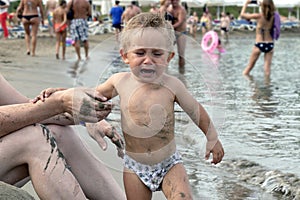 Beautiful baby crying on the beach. A 1-2 year old child holds father by the hand and cries.