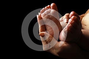 Beautiful baby baby feet on the handle of the parent hands on a black background