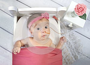 Beautiful baby girl with feeding tube in doll bed