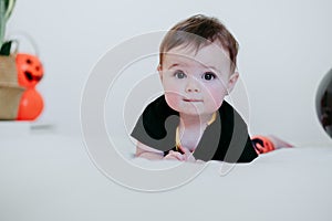 Beautiful baby girl in halloween costume at home, sitting on bed with Halloween decoration, Lifestyle indoors