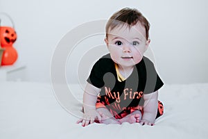 Beautiful baby girl in halloween costume at home, sitting on bed with Halloween decoration, Lifestyle indoors