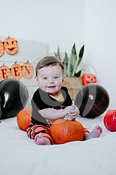 Beautiful baby girl in halloween costume at home, sitting on bed with Halloween decoration, Lifestyle indoors